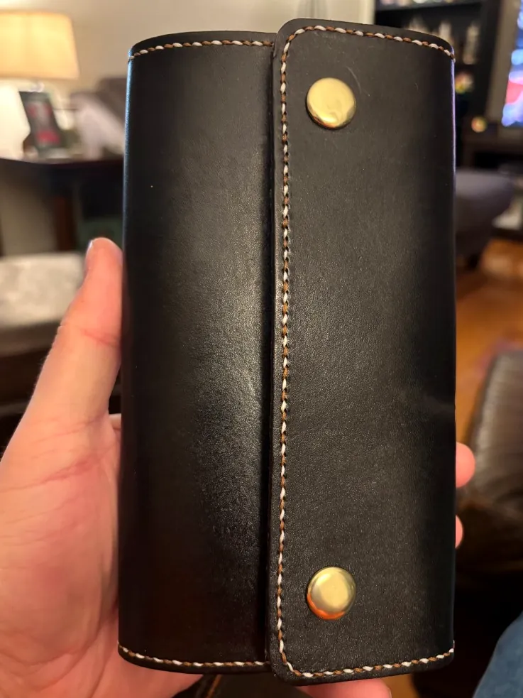 Black leather clutch wallet with dual-color saddle stitch and two brass snaps
