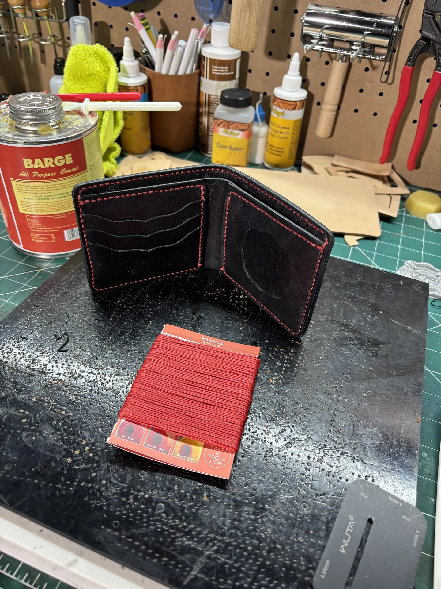 Handmade Corbett & Co. leather wallet on the workbench with tools and thread